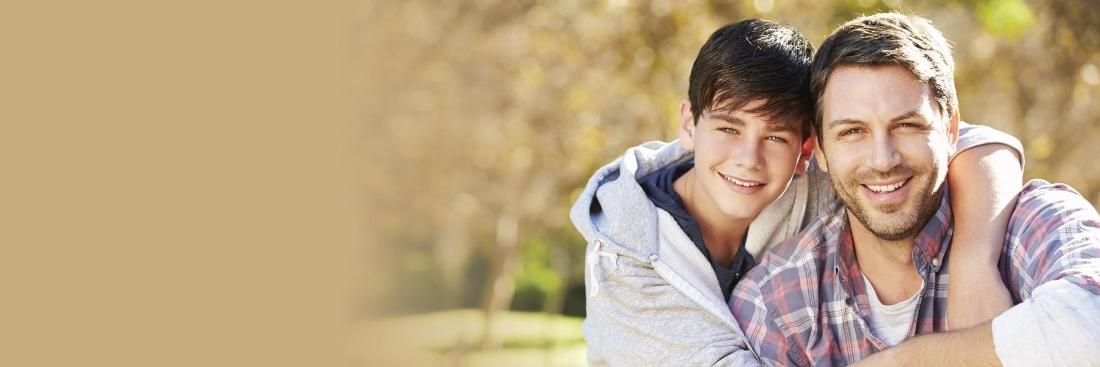 dark haired father and son smiling against a fading autumn outdoor area