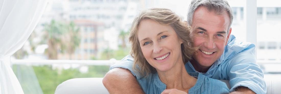 older man and woman hugging on a screened in porch while looking forward and smiling