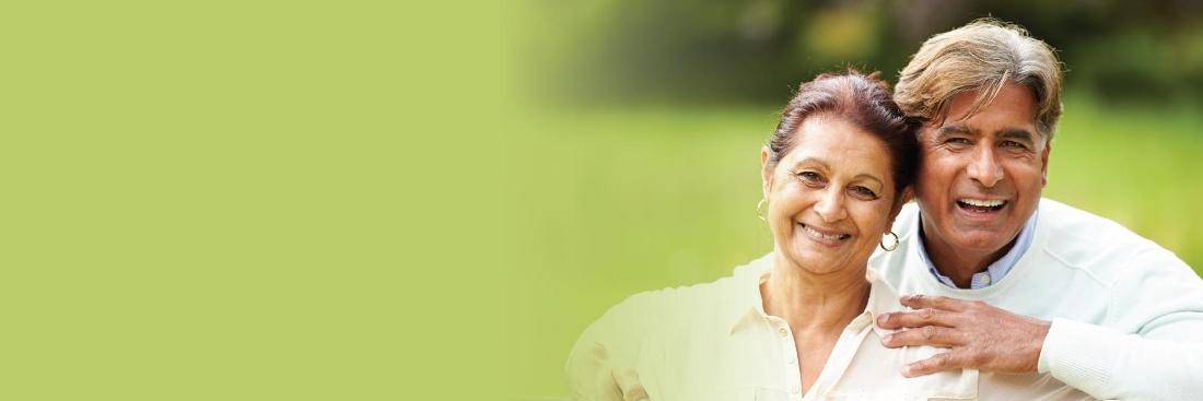 elderly dark haired man and woman smiling against a green outdoor spring background
